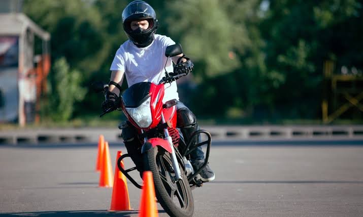 Aluno em aula prática de moto entre cones em pista de autoescola