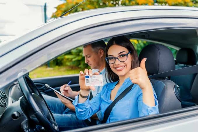 Aluna sorrindo dentro do carro exibindo sua carteira de habilitação